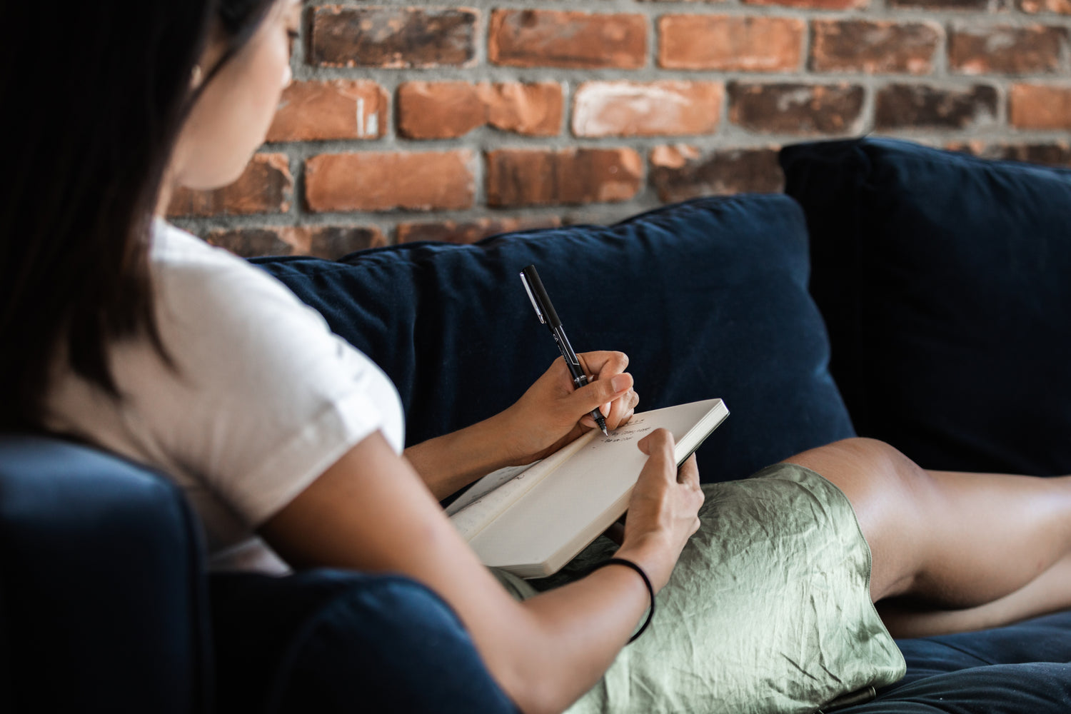 Woman writing in her journal while relaxing on the couch