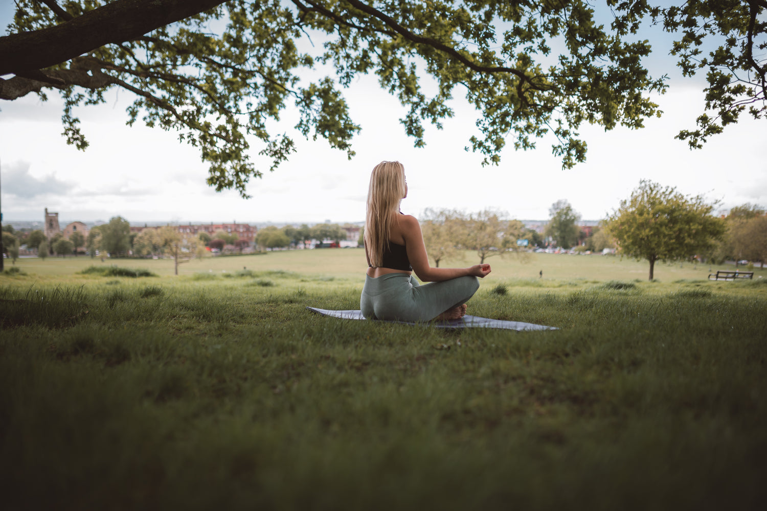 Woman sitting out in a field, meditating under a tree